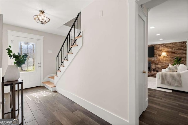 foyer entrance with recessed lighting, brick wall, dark wood-style flooring, baseboards, and stairway