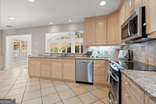 kitchen with stainless steel appliances, light brown cabinets, a sink, and decorative backsplash