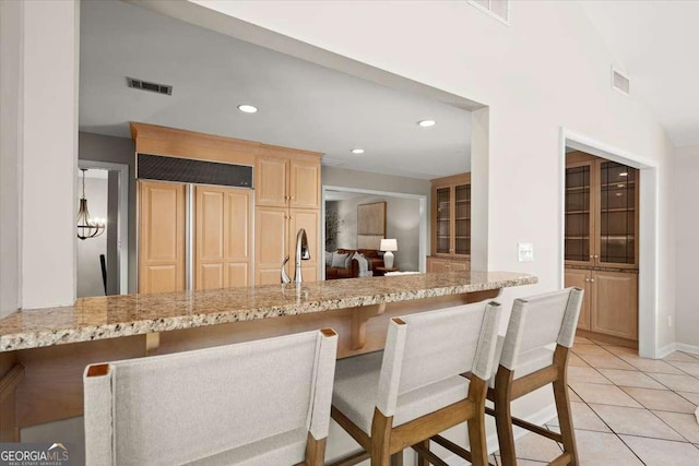 kitchen with a breakfast bar, visible vents, light tile patterned flooring, and light brown cabinetry