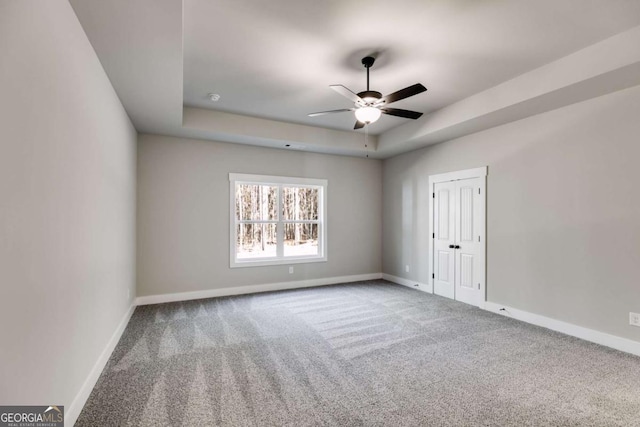 empty room featuring carpet floors, a raised ceiling, baseboards, and a ceiling fan