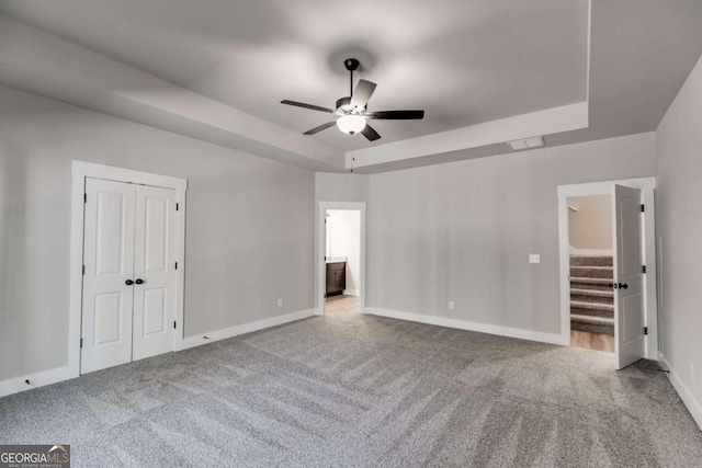 unfurnished bedroom featuring ensuite bathroom, carpet floors, baseboards, a closet, and a tray ceiling