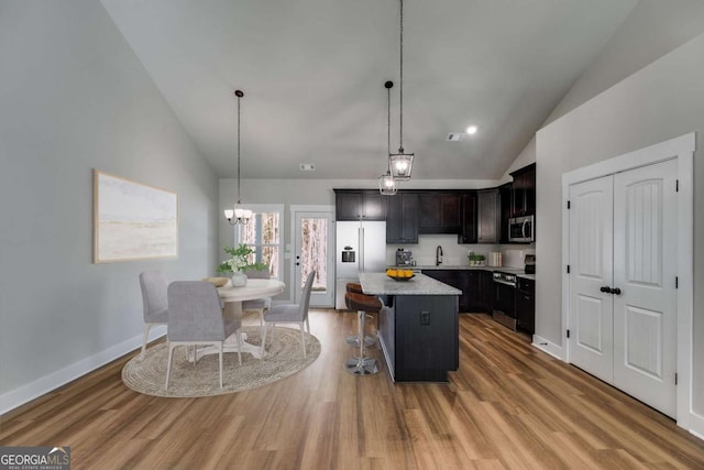 kitchen featuring light wood-style flooring, stainless steel appliances, a sink, a kitchen island, and a kitchen bar