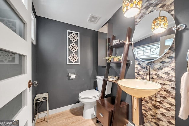 half bath featuring visible vents, toilet, and wood finished floors