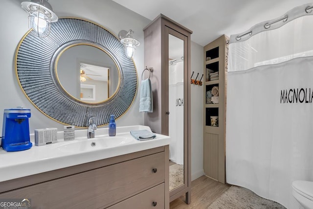 bathroom featuring vanity, a ceiling fan, toilet, curtained shower, and wood finished floors