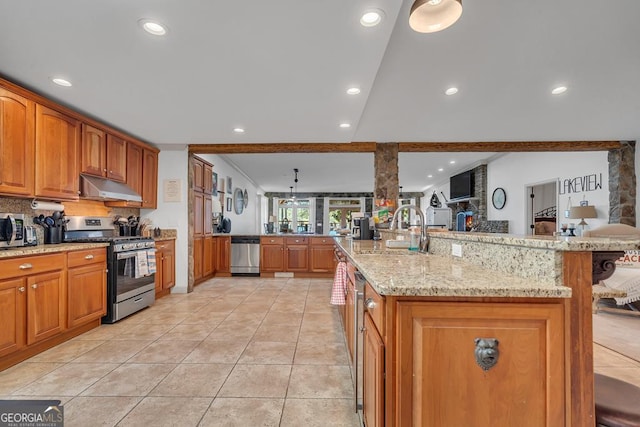 kitchen featuring a sink, appliances with stainless steel finishes, under cabinet range hood, brown cabinets, and light stone counters