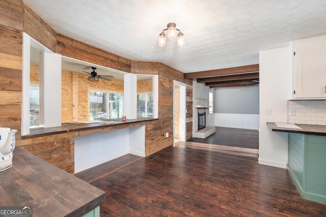 kitchen with a fireplace, dark wood-type flooring, white cabinets, wood walls, and a textured ceiling