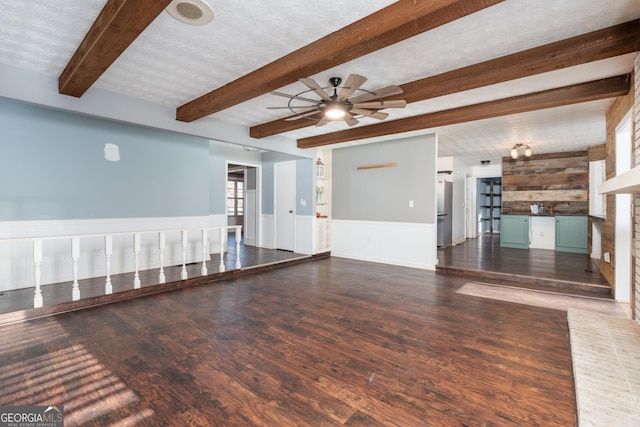 unfurnished living room featuring a textured ceiling, a wainscoted wall, wood finished floors, a ceiling fan, and beamed ceiling