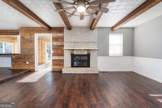 unfurnished living room with a textured ceiling, a wainscoted wall, a brick fireplace, and wood finished floors