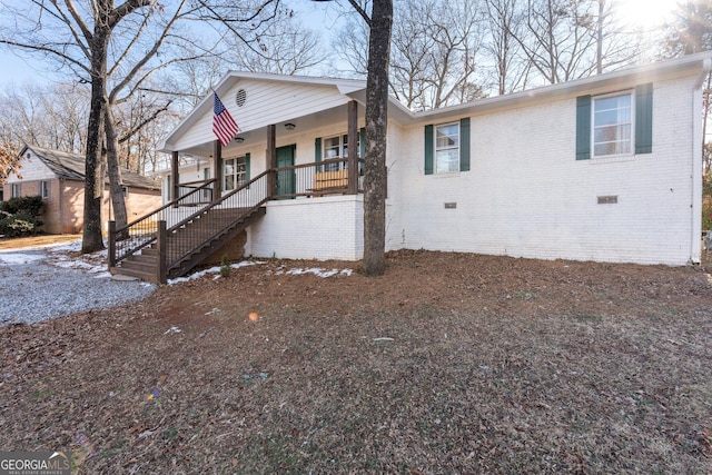 view of front of house with covered porch, brick siding, crawl space, and stairway