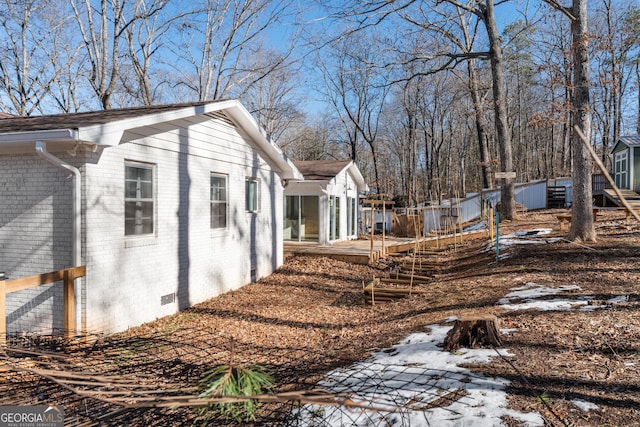 view of home's exterior featuring brick siding, crawl space, an outdoor structure, and fence