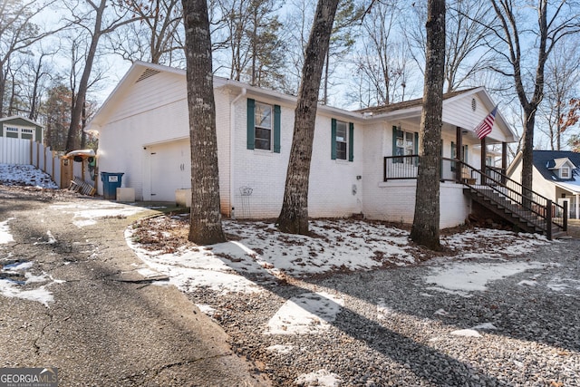 view of snowy exterior featuring a porch, a garage, brick siding, driveway, and stairway