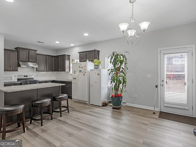 kitchen with light wood finished floors, tasteful backsplash, dark brown cabinets, white appliances, and under cabinet range hood