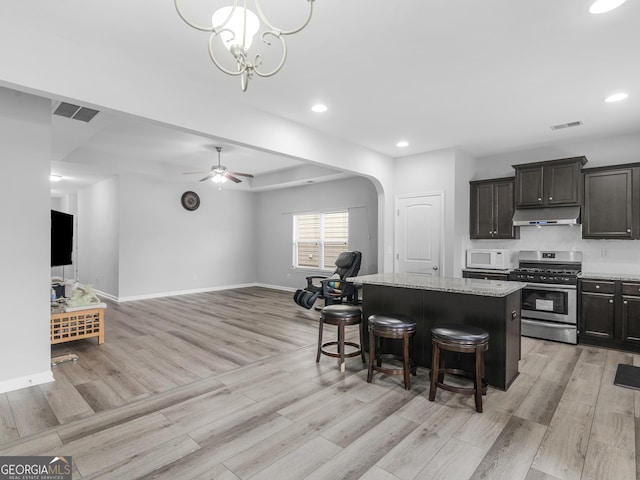 kitchen featuring arched walkways, white microwave, stainless steel range with gas stovetop, a kitchen island, and under cabinet range hood