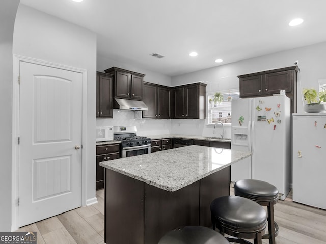 kitchen featuring white appliances, light wood finished floors, visible vents, under cabinet range hood, and a sink