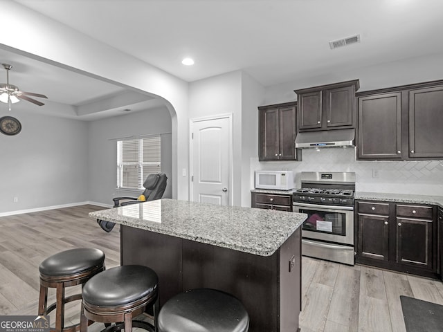 kitchen featuring visible vents, arched walkways, white microwave, under cabinet range hood, and stainless steel range with gas cooktop