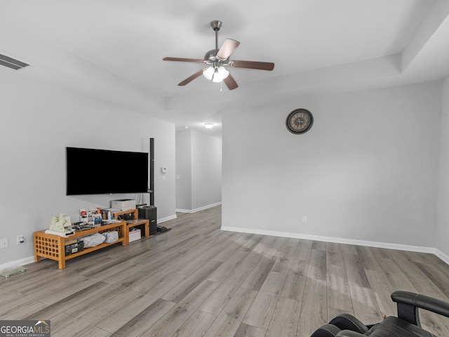 unfurnished living room featuring a raised ceiling, visible vents, a ceiling fan, wood finished floors, and baseboards