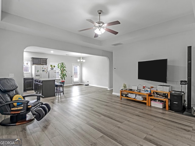 living room with light wood-style floors, arched walkways, visible vents, and a tray ceiling