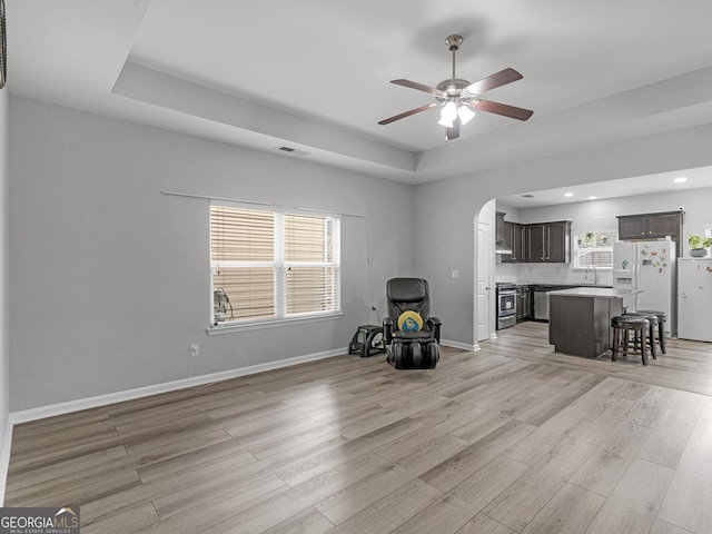 unfurnished living room featuring baseboards, visible vents, a raised ceiling, light wood-style floors, and a sink