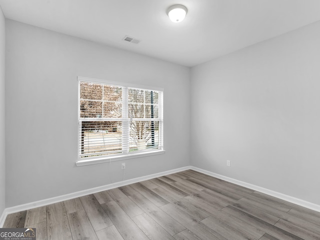 spare room with baseboards, visible vents, and wood finished floors