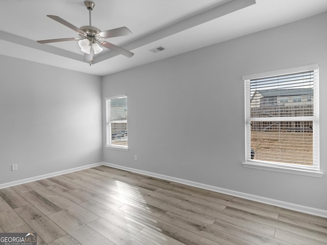 empty room with a raised ceiling, visible vents, baseboards, and wood finished floors