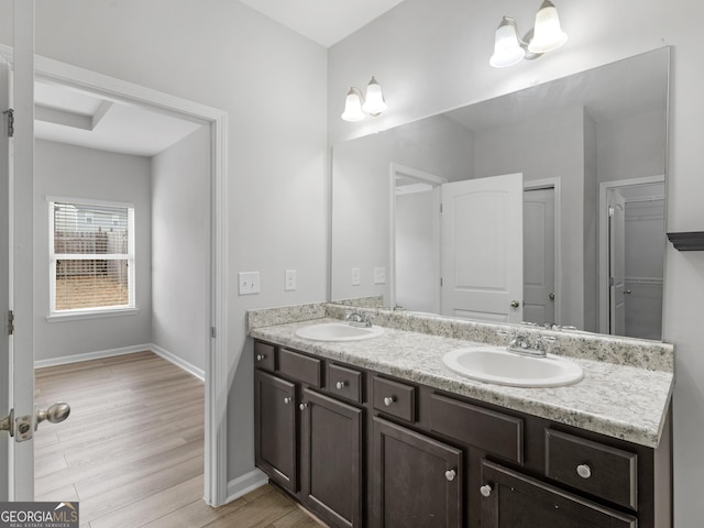 full bathroom with double vanity, baseboards, a sink, and wood finished floors