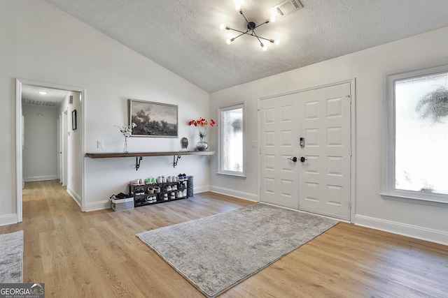 foyer with lofted ceiling, visible vents, a textured ceiling, wood finished floors, and baseboards