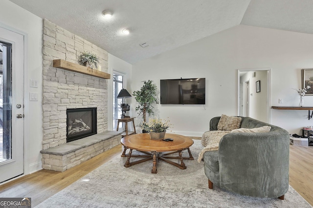 living area with lofted ceiling, visible vents, wood finished floors, and a stone fireplace