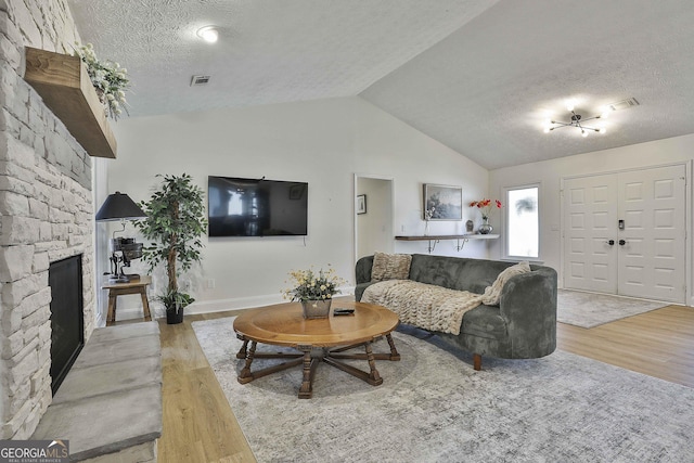 living room featuring a textured ceiling, a fireplace, wood finished floors, visible vents, and vaulted ceiling