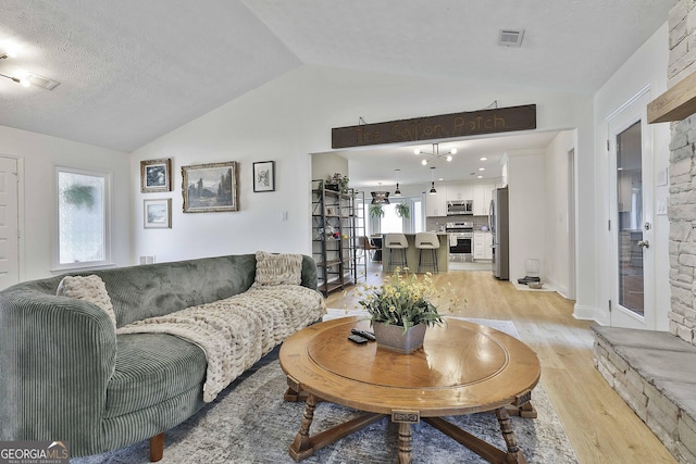 living room with lofted ceiling, visible vents, a textured ceiling, and light wood-style flooring