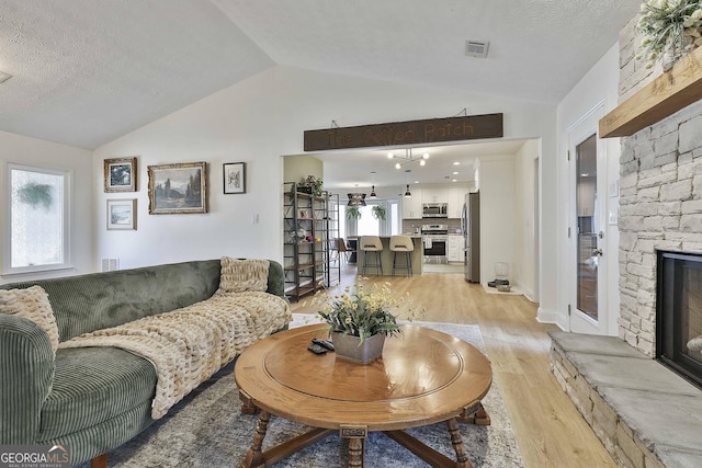 living area featuring visible vents, lofted ceiling, a textured ceiling, light wood-style floors, and a fireplace