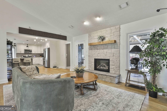 living room featuring light wood-style flooring, a fireplace, visible vents, baseboards, and vaulted ceiling