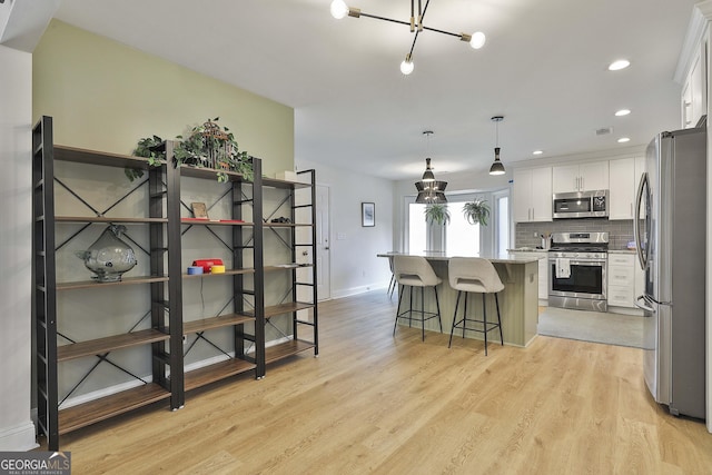 kitchen with stainless steel appliances, a kitchen breakfast bar, white cabinets, decorative backsplash, and light wood finished floors