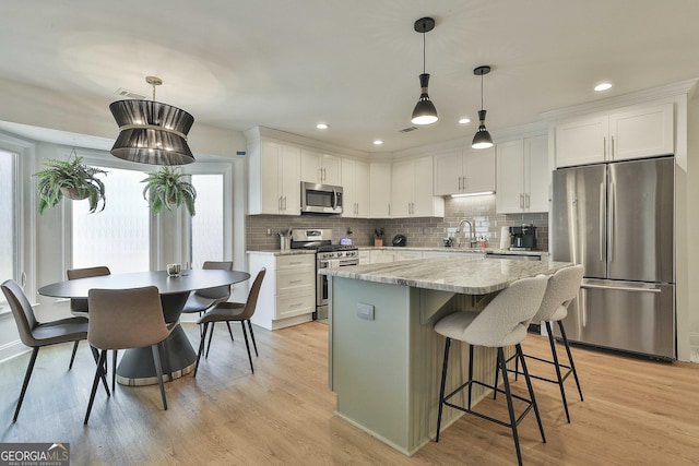 kitchen featuring stainless steel appliances, white cabinets, light wood-style floors, a center island, and pendant lighting