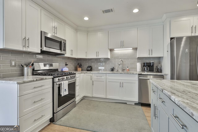 kitchen featuring visible vents, appliances with stainless steel finishes, light stone countertops, white cabinetry, and a sink