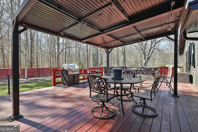 wooden deck featuring a grill, fence, a view of trees, and outdoor dining space