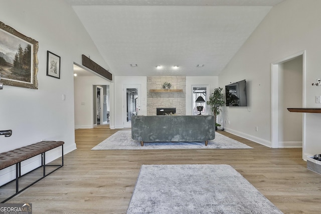 living room featuring lofted ceiling, baseboards, wood finished floors, and a stone fireplace