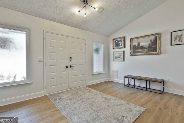 foyer featuring baseboards, visible vents, lofted ceiling, a textured ceiling, and light wood-style floors