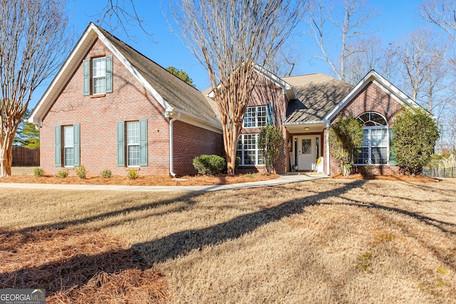 traditional-style house with brick siding, roof with shingles, a front yard, and fence