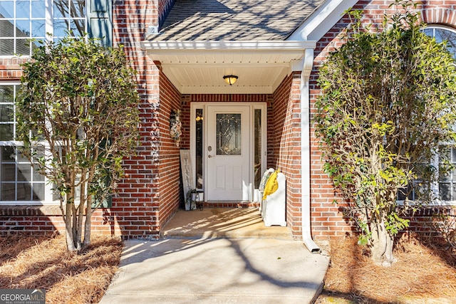 view of exterior entry featuring roof with shingles and brick siding