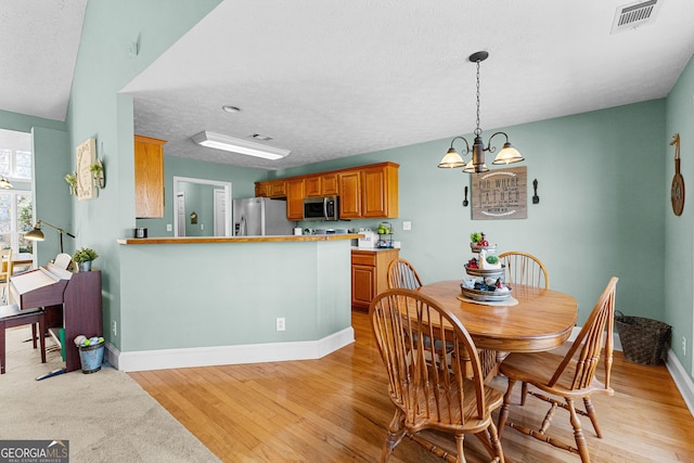 dining area featuring a textured ceiling, light wood finished floors, visible vents, and baseboards