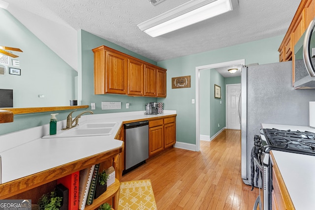 kitchen featuring appliances with stainless steel finishes, brown cabinets, light countertops, light wood-type flooring, and a sink