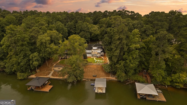 aerial view at dusk with a water view and a wooded view