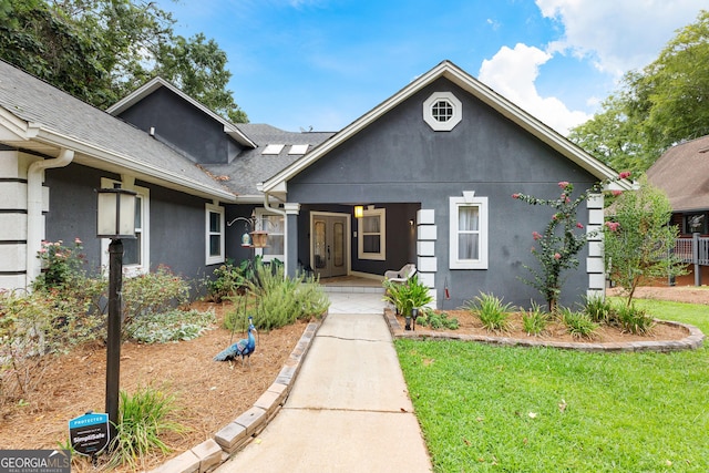 view of front of property featuring a front lawn, roof with shingles, a porch, and stucco siding