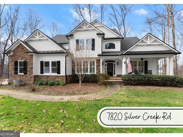 craftsman-style home featuring ceiling fan, covered porch, stone siding, a standing seam roof, and a front yard