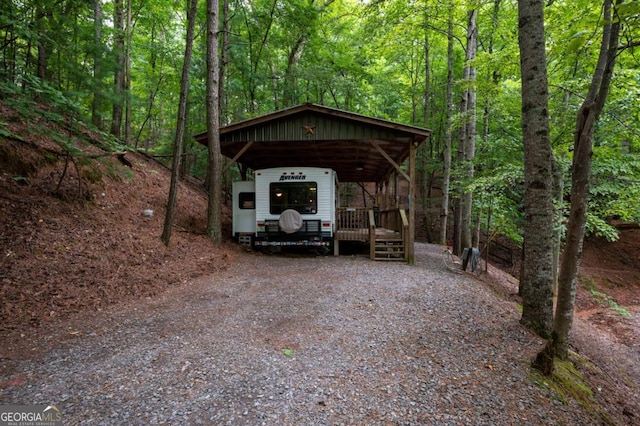 view of parking featuring gravel driveway, a view of trees, and a detached carport