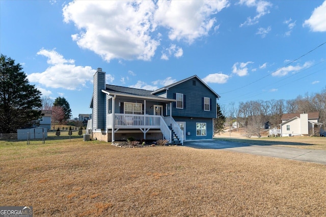 tri-level home featuring a chimney, a porch, a front yard, fence, and driveway