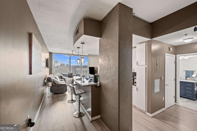 corridor featuring light wood finished floors, visible vents, expansive windows, and baseboards