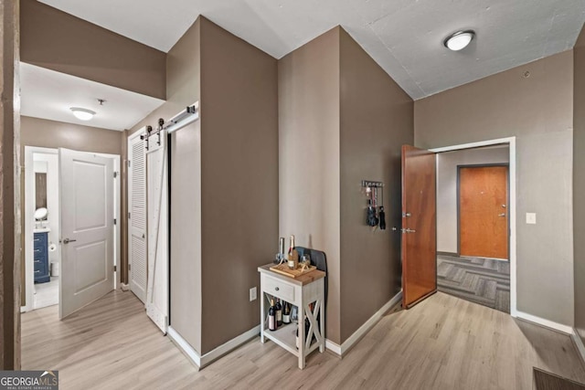 corridor with light wood-style flooring, baseboards, and a barn door