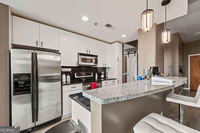 kitchen with a barn door, stainless steel appliances, a peninsula, white cabinetry, and decorative backsplash