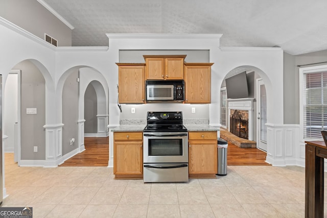 kitchen featuring stainless steel electric range, light stone counters, a fireplace, and light tile patterned flooring